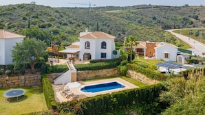 A residential property with a swimming pool, a covered patio, and a view of a hilly landscape.