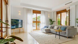 A modern living room with a grey sofa, a TV on a stand, and a large window with curtains.