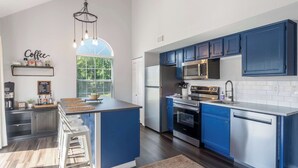 A modern kitchen with blue cabinets, a central island, and a coffee station. - The Lazy Loft Stay for 4! (Branson)