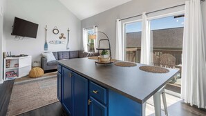 A modern kitchen with a large island, a flat-screen TV mounted on the wall, and a dining area with a view of the outside. - The Lazy Loft Stay for 4! (Branson)