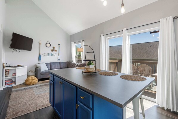 A modern kitchen with a large island, a flat-screen TV mounted on the wall, and a dining area with a view of the outside.