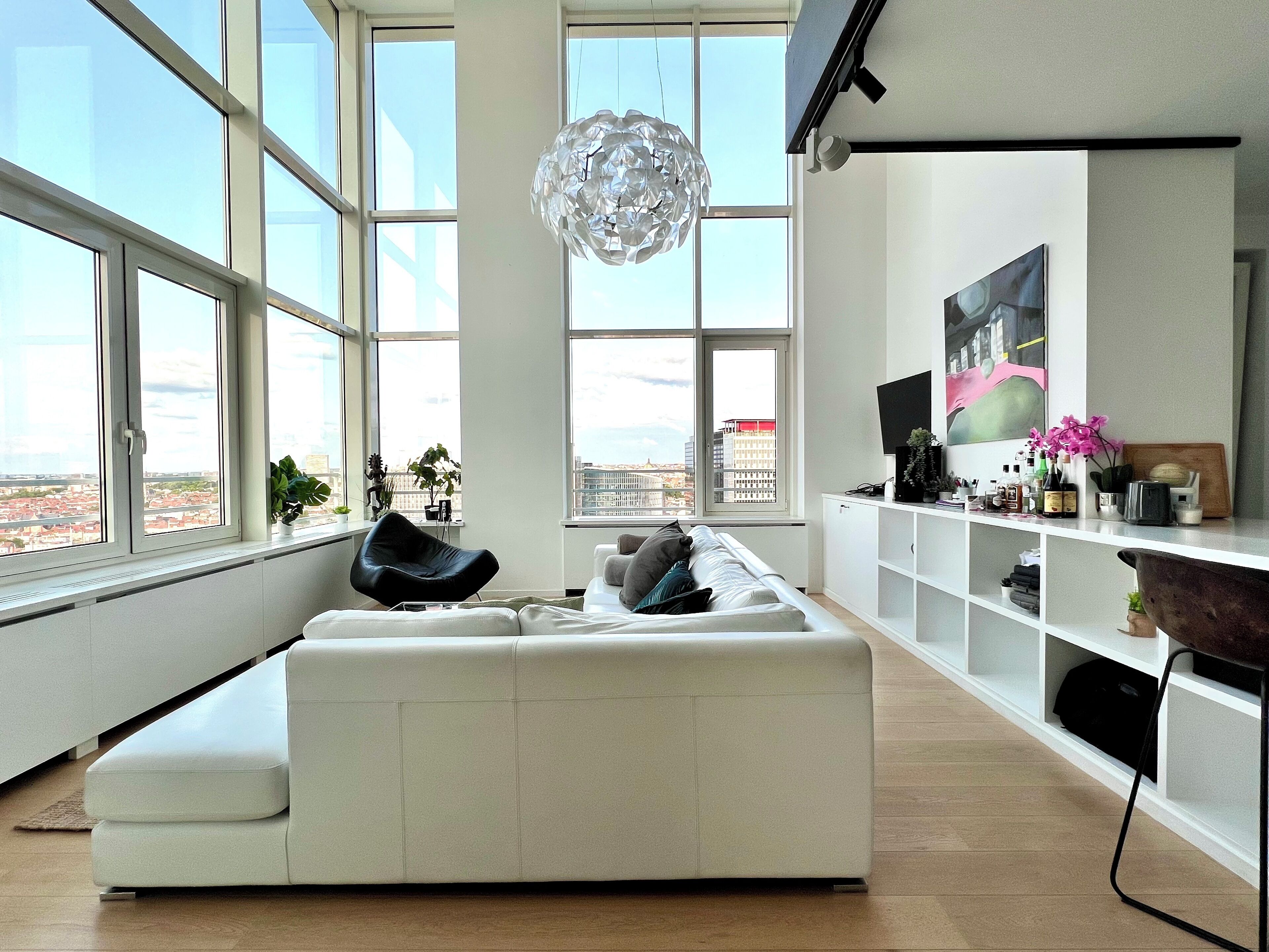 A modern living room with a white sofa, a black chair, and a large window offering a city view.