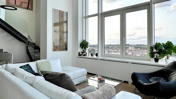 Ein modernes Wohnzimmer mit einem weißen Ledersofa, einem schwarzen Ledersessel, einem Glastisch und einem großen Fenster mit Blick auf die Stadt.