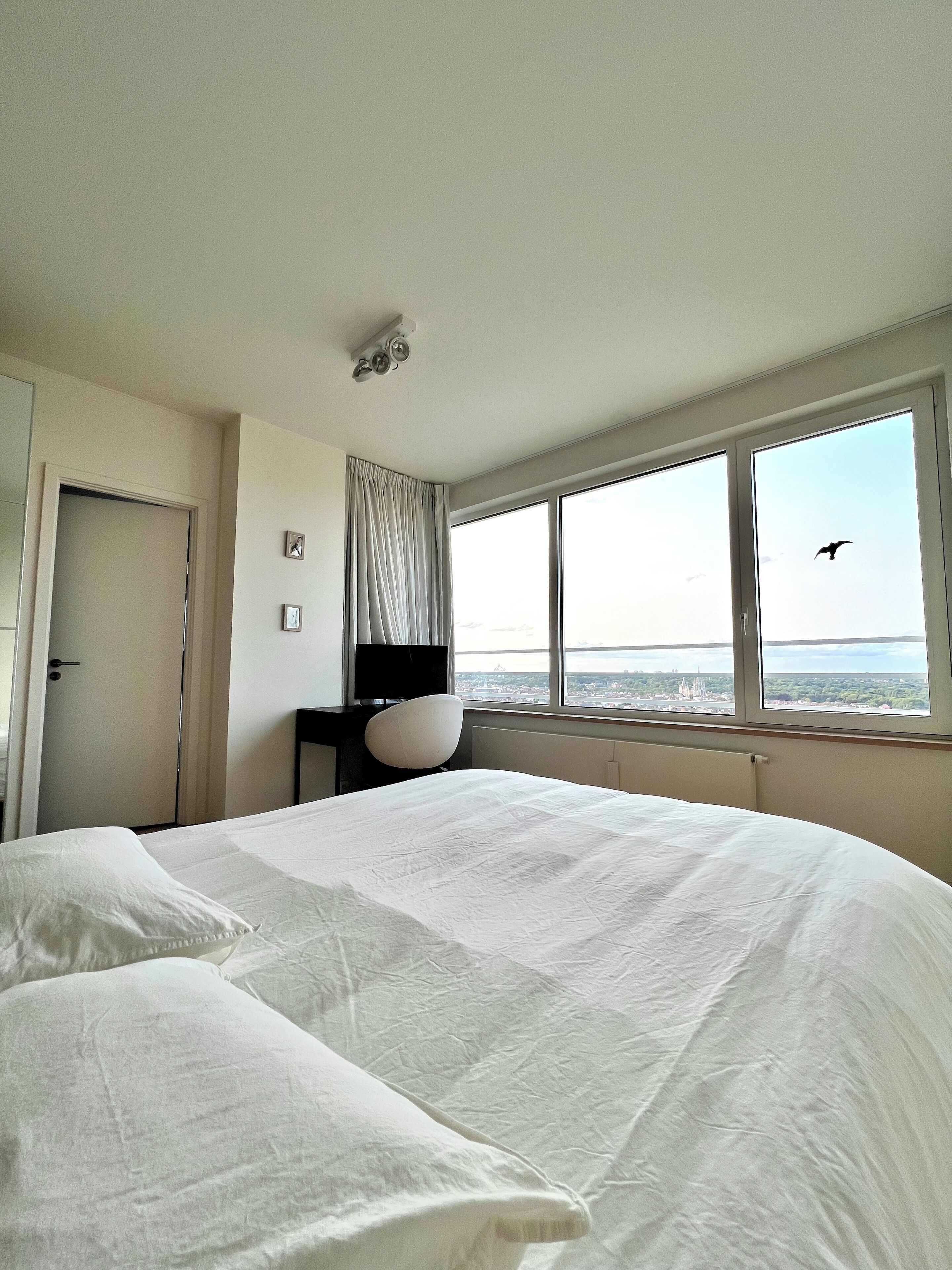Habitación de hotel con una cama grande, una silla, un escritorio y una ventana con vistas a la ciudad.