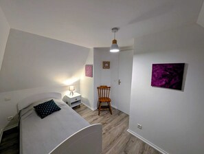 Een slaapkamer met een bed, nachtkastje, stoel en een deur naar een andere kamer.