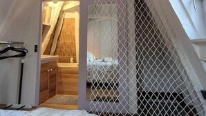 Een slaapkamer met schuine wand, houten vloer, een bed en een kleine badkamer met douche.
