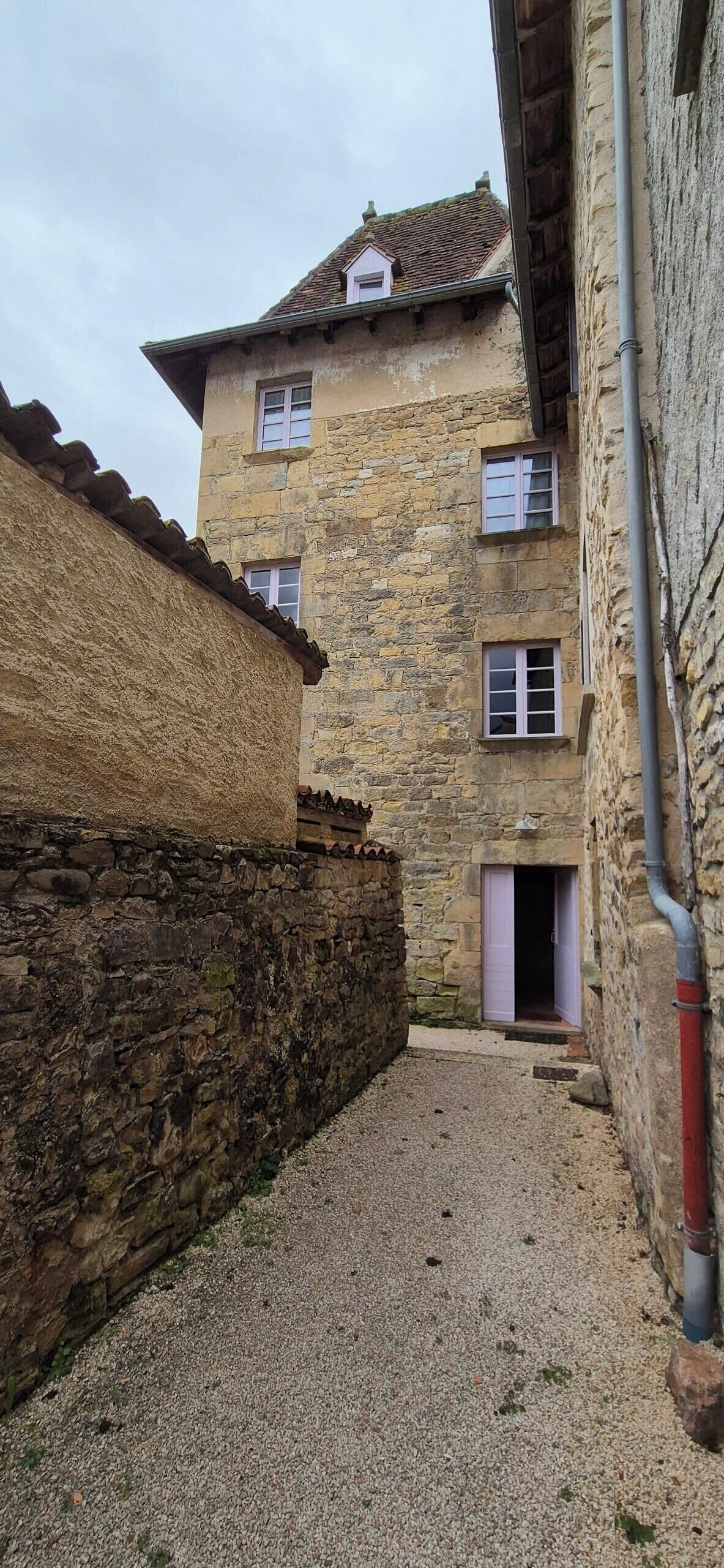 A narrow alleyway with stone buildings, one with a visible door and window, and a gravel path.