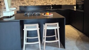 Une cuisine moderne avec un mur de pierre en guise de crédence, un îlot central doté de tabourets et des appareils électroménagers intégrés.