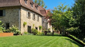 Un bâtiment en pierre avec un toit en pente, de nombreuses fenêtres et une pelouse bien entretenue.