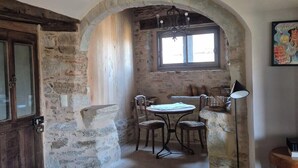 Un intérieur rustique avec une arche en pierre menant à un espace repas agrémenté de meubles en bois et d’une table.