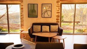 Un intérieur moderne avec un canapé, une table ronde et une petite table d’appoint. Deux grandes fenêtres offrent une vue sur l’extérieur.