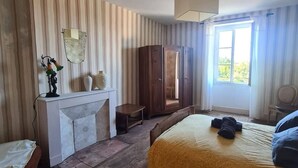 A bedroom with a bed, a wardrobe, a mirror, a fireplace, and a window. - Chez Mamie, Gramat centre (Gramat)