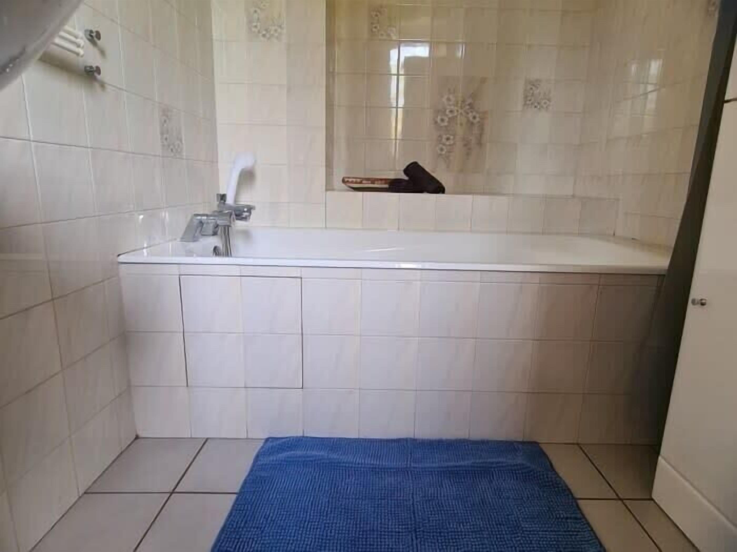 A bathroom with a white bathtub, a blue towel on the floor, and a towel rack on the wall.