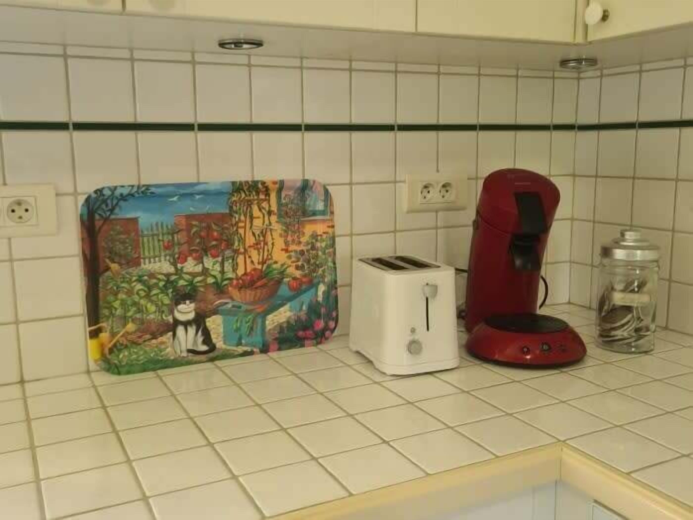 A kitchen with white tiles, a toaster, a red coffee maker, and a colorful cutting board.