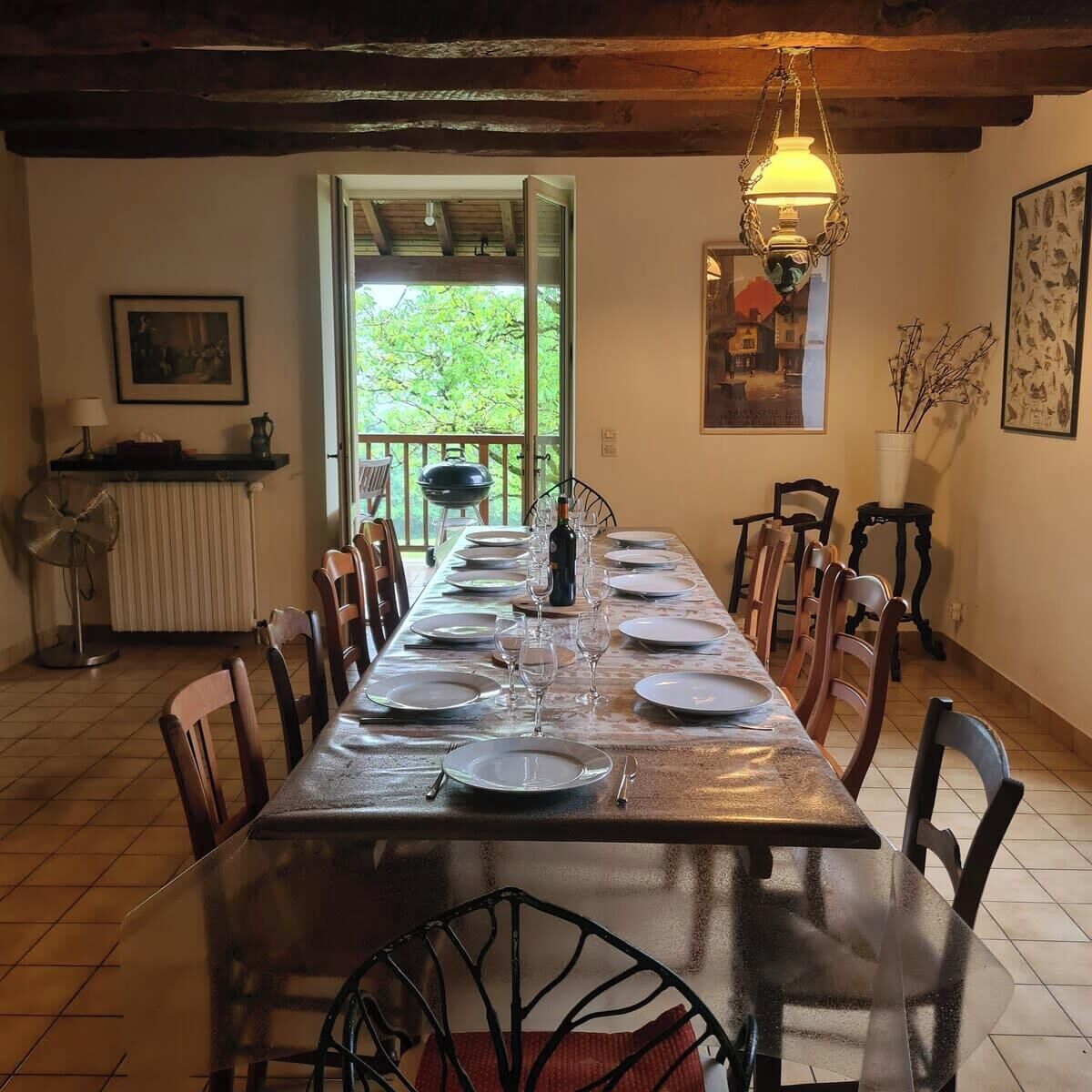 A dining room with a long table set for a meal, chairs around it, a fan, a radiator, and a view of the outdoors.
