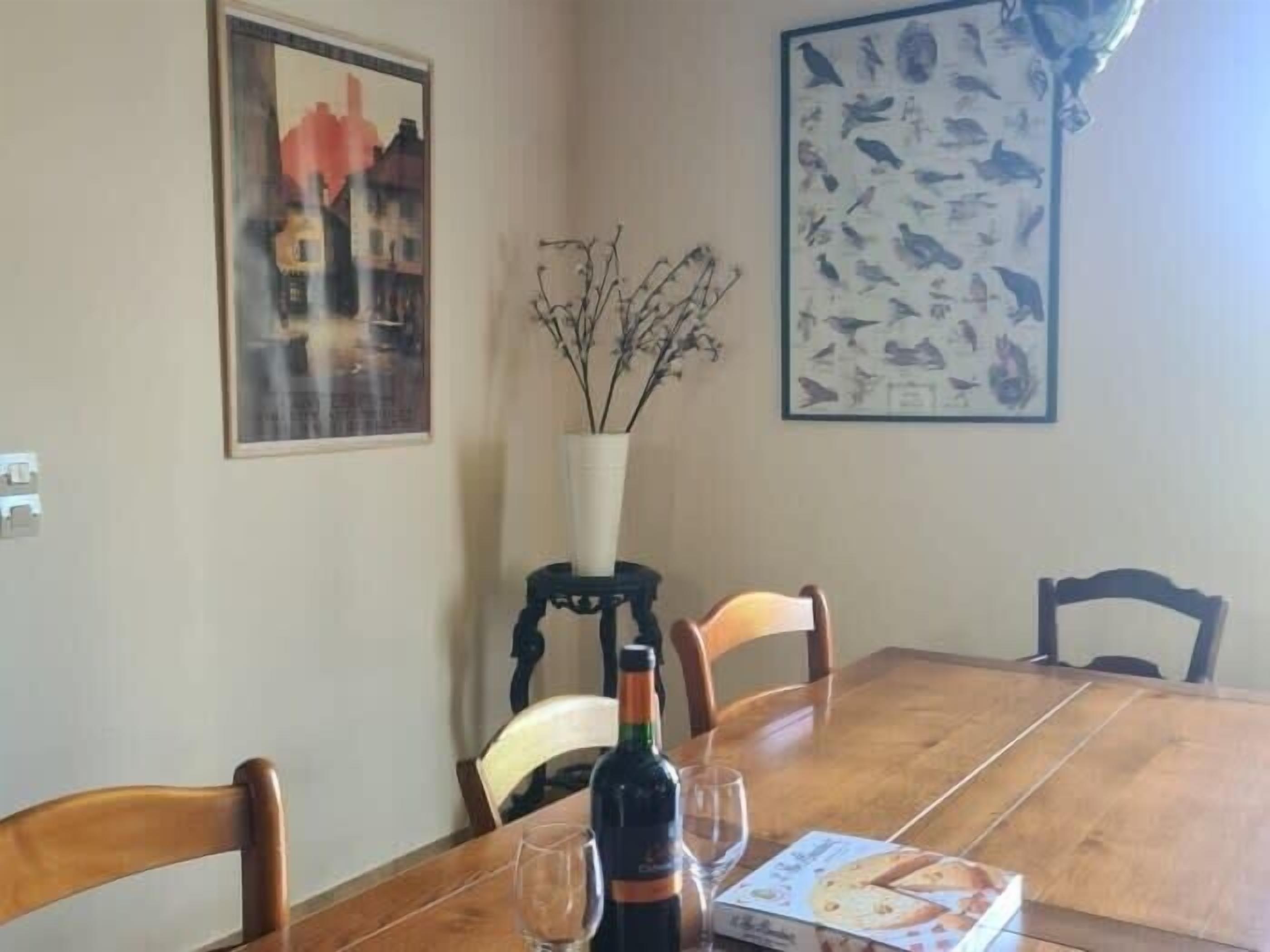 Une table à manger avec des chaises, une bouteille de vin, un verre et une boîte de crackers.