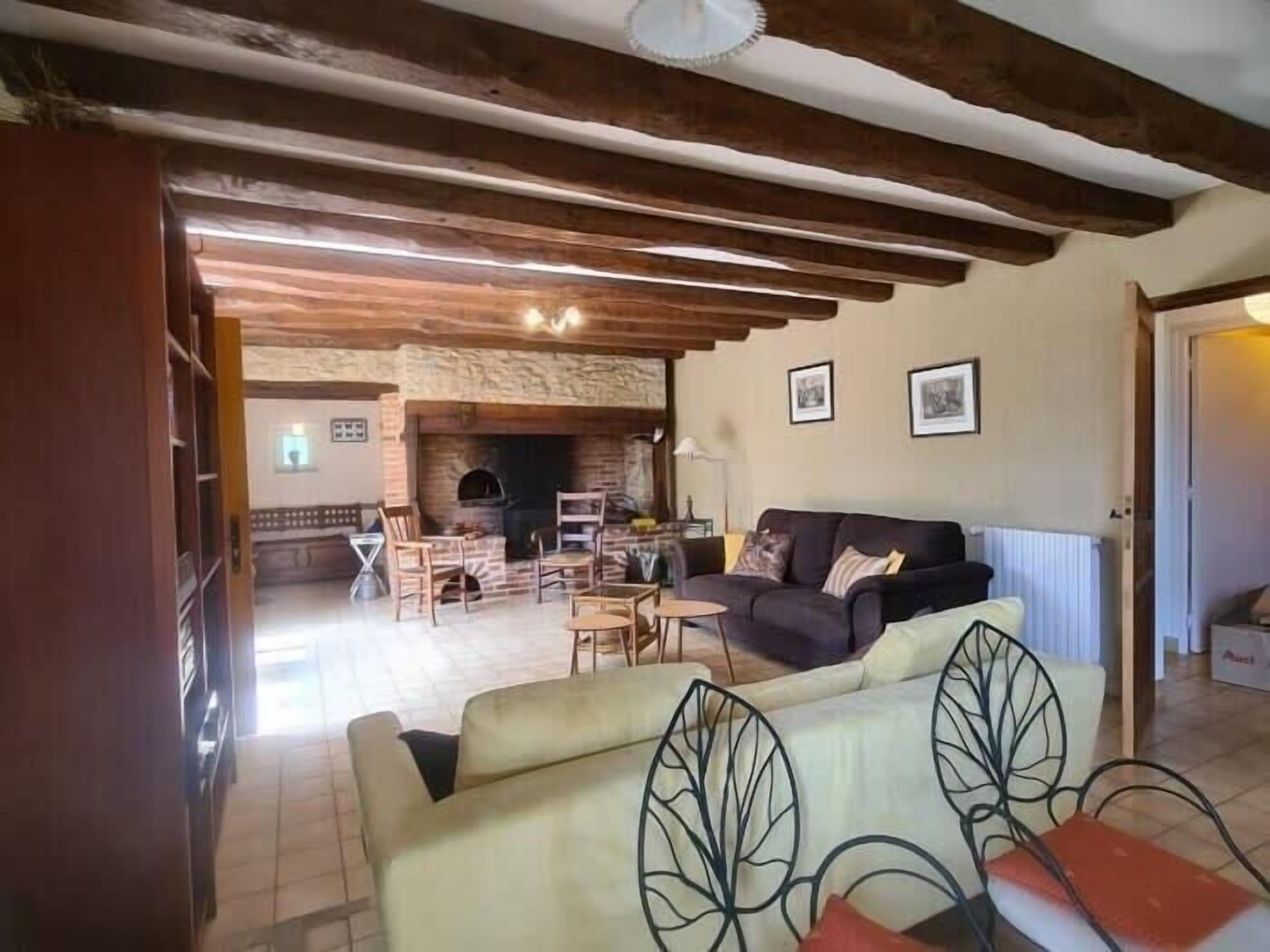 A rustic living room with exposed wooden beams, a stone fireplace, and a sofa with leaf-patterned cushions.