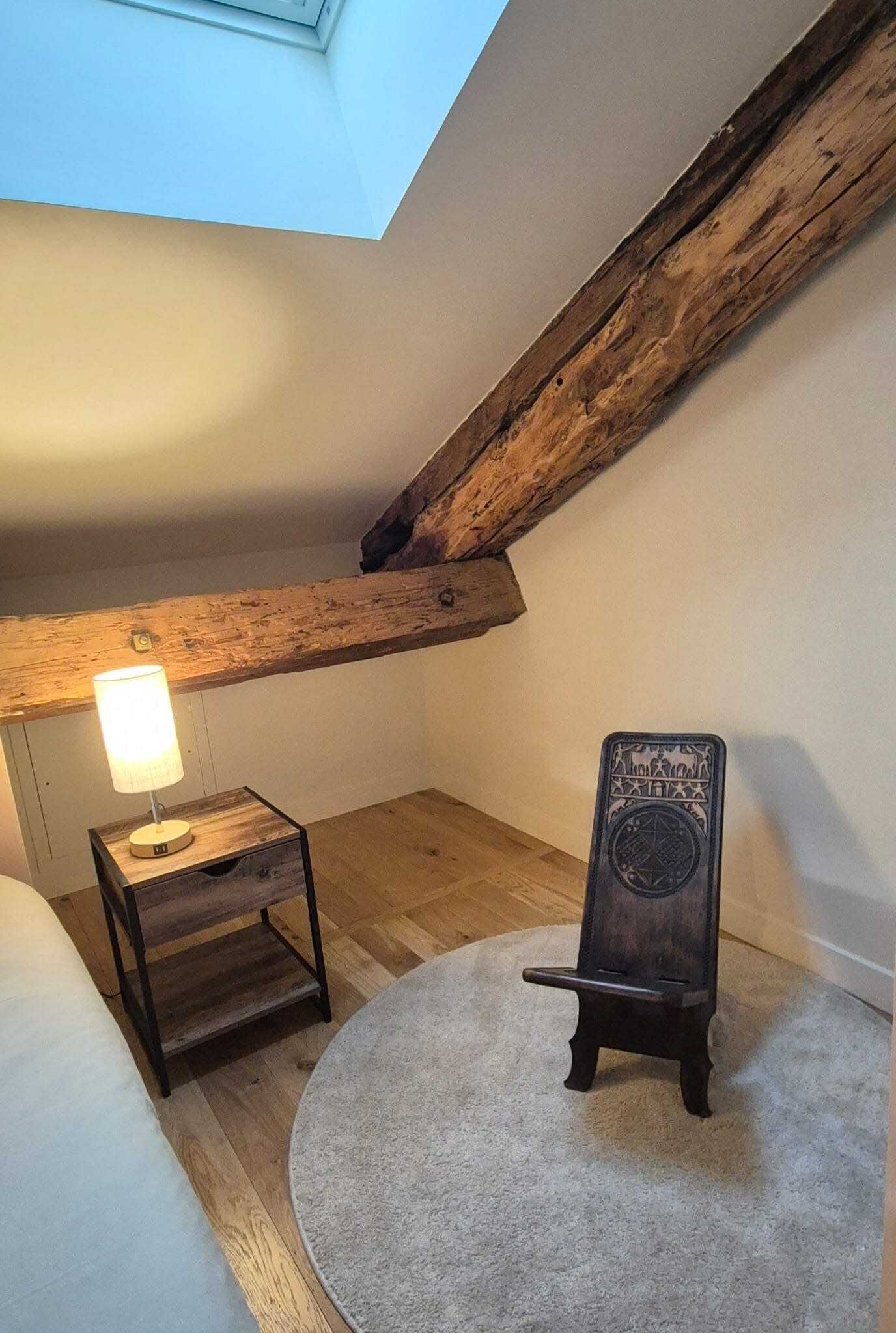Un dormitorio estilo loft acogedor con tragaluz, una pequeña mesa de madera con lámpara, y una pizarra.