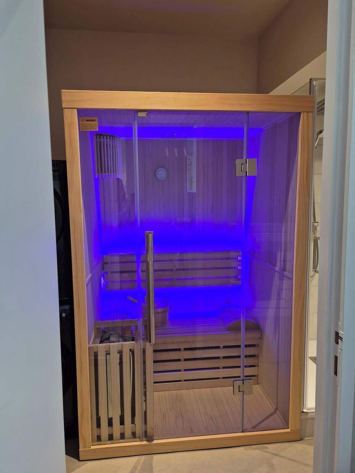 A sauna with a wooden interior, glass walls, and a blue light.