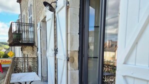 Un estrecho pasillo exterior con suelo de piedra, una pequeña mesa y una barandilla de metal.