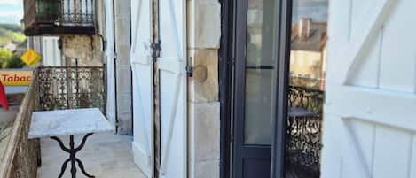 A narrow outdoor corridor with a stone floor, a small table, and a metal railing.