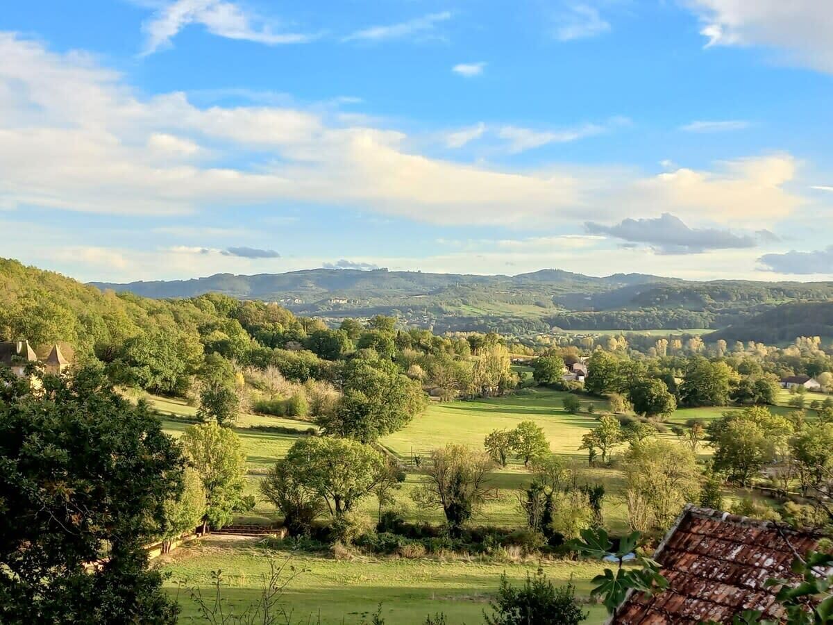 Un paysage rural caractérisé par des collines douces, des arbres dispersés et quelques bâtiments visibles au loin.