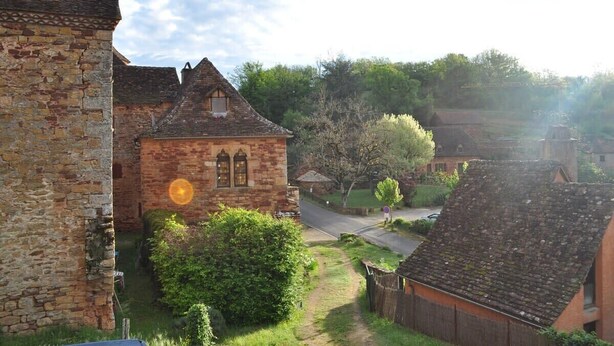 A traditional stone building with a steeply pitched roof, surrounded by lush greenery and a clear sky.