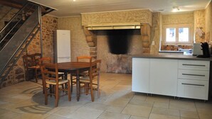 A kitchen with a stone wall, a fireplace, a dining table with chairs, and a staircase.