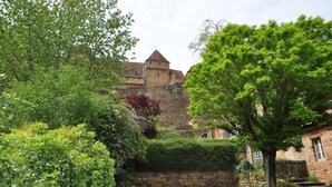 A historic stone building with a tower, surrounded by lush greenery and a stone wall.