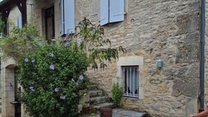 A stone building with a rustic exterior, a small garden with purple flowers, and a metal railing on the steps.