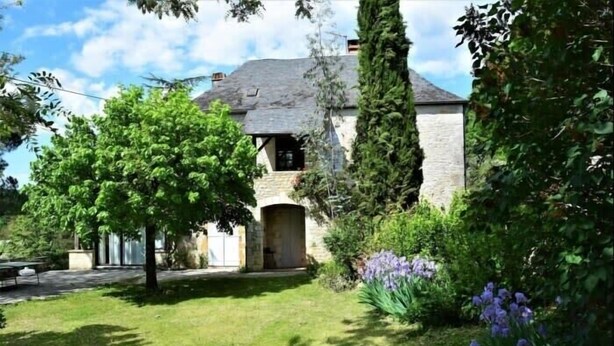 A stone building with a sloped roof, surrounded by lush greenery and trees.
