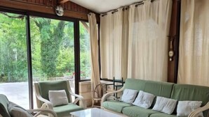 A room with a green sofa, two white armchairs, a white coffee table, and large windows with curtains.