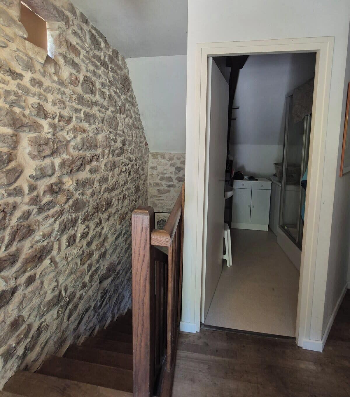 A staircase with a stone wall on one side and a doorway leading to a bathroom with a sink and cabinets.