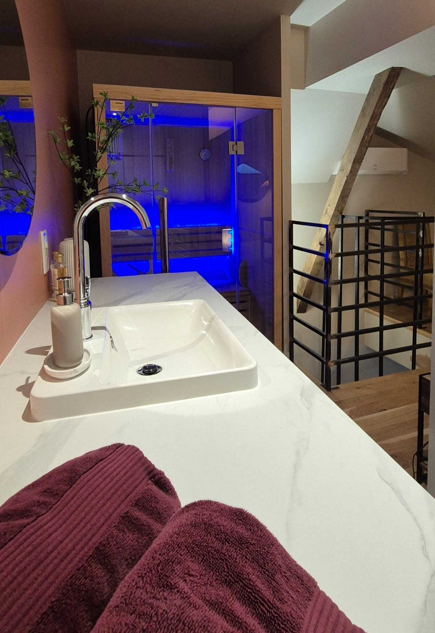 A modern bathroom with a white sink, a mirror, and a wooden staircase.