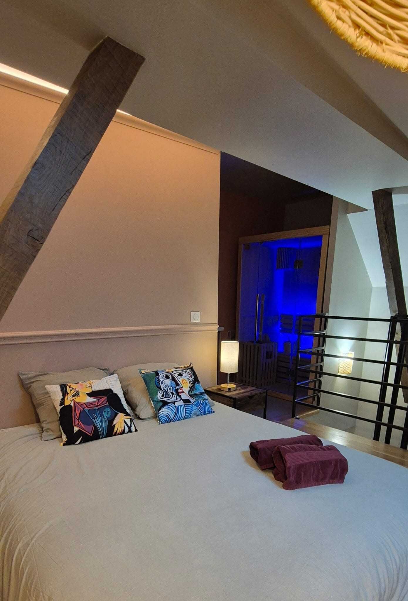 Une chambre à coucher avec un grand lit, deux oreillers ornés de motifs colorés, une lampe de chevet et une vue sur un balcon doté d’une balustrade.