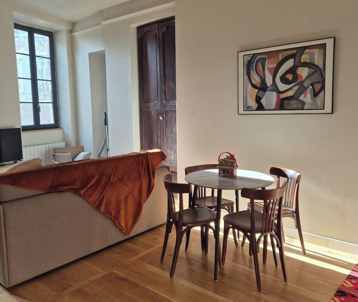 A living room with a sofa, a dining table with chairs, a TV, and a window.