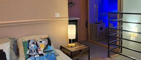 A bedroom with a bed, pillows, a nightstand, a lamp, a wooden floor, and a view of a balcony with a railing.