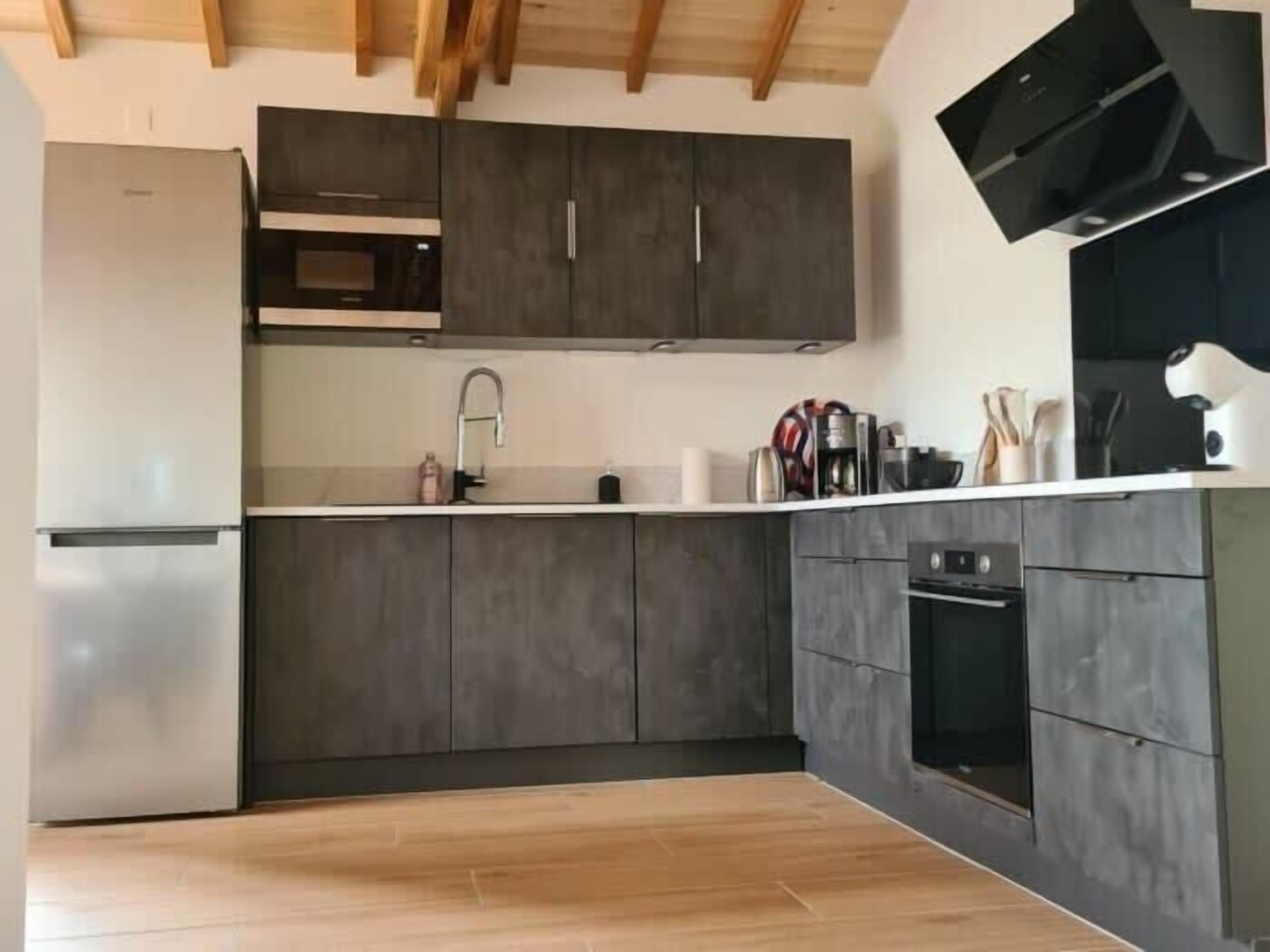 Een moderne keuken met donkere kastjes, een roestvrijstalen koelkast, een magnetron, een koffiezetapparaat en een inbouwoven.