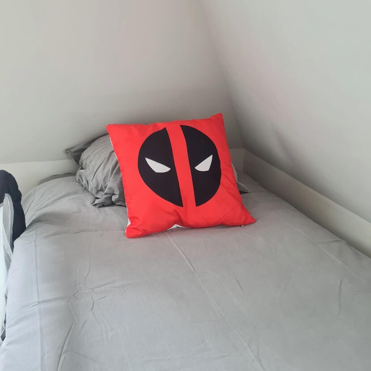 A bed with a grey mattress and a red pillow featuring a black and white design.