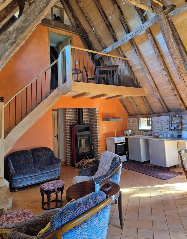 Un loft amplio con techos altos, vigas de madera a la vista, una zona de estar acogedora con sofás y una mesa de centro, una cocina con electrodomésticos modernos y una chimenea.