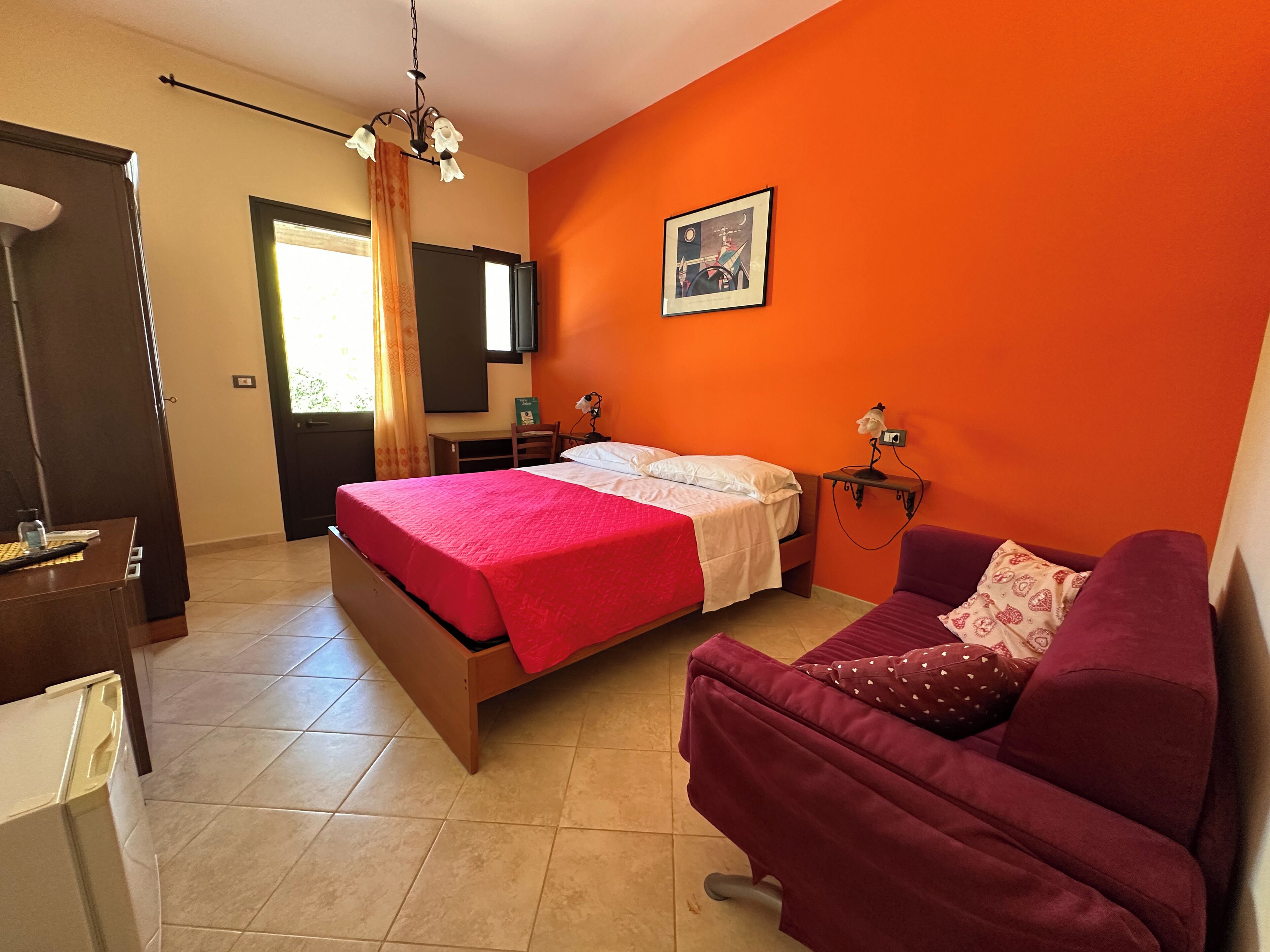 A bedroom with a bed, a desk, a chair, a sofa, a TV, and a painting on the wall.