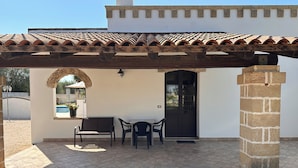 A covered patio area with a table and chairs, a bench, and a door. - LA PALMA VACANZE (Sogliano Cavour)