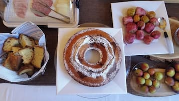 Una mesa con diversos alimentos, incluyendo un pastel bundt, papas asadas y un tazón de fruta.
