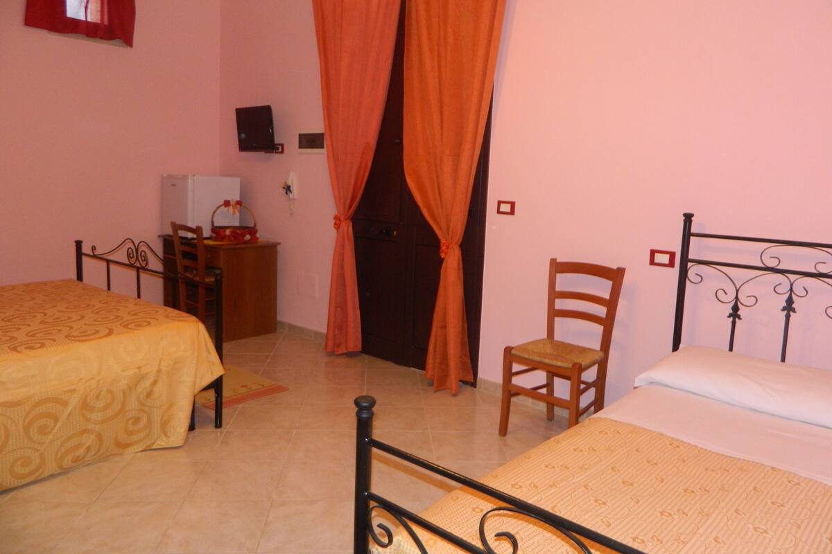 A bedroom with two beds, a wooden chair, a desk with a computer, and a TV on the wall.