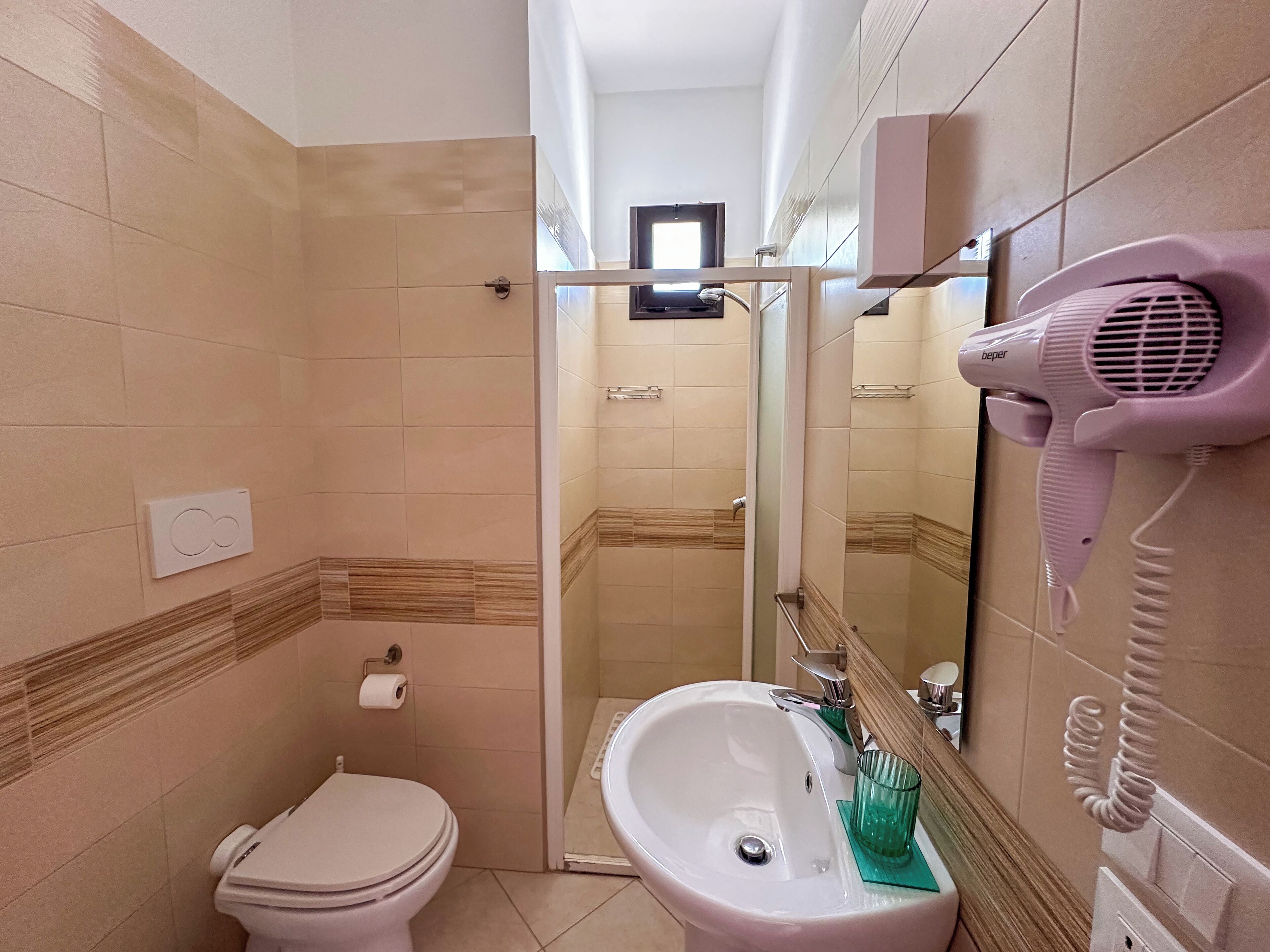 Un baño con inodoro, lavamanos y un secador de pelo montado en la pared.
