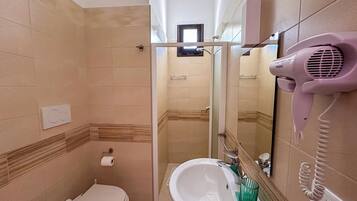 Un baño con inodoro, lavamanos y un secador de pelo montado en la pared.