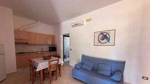 A compact living space with a kitchenette, a dining table with chairs, and a blue sofa. - LA PALMA VACANZE (Sogliano Cavour)