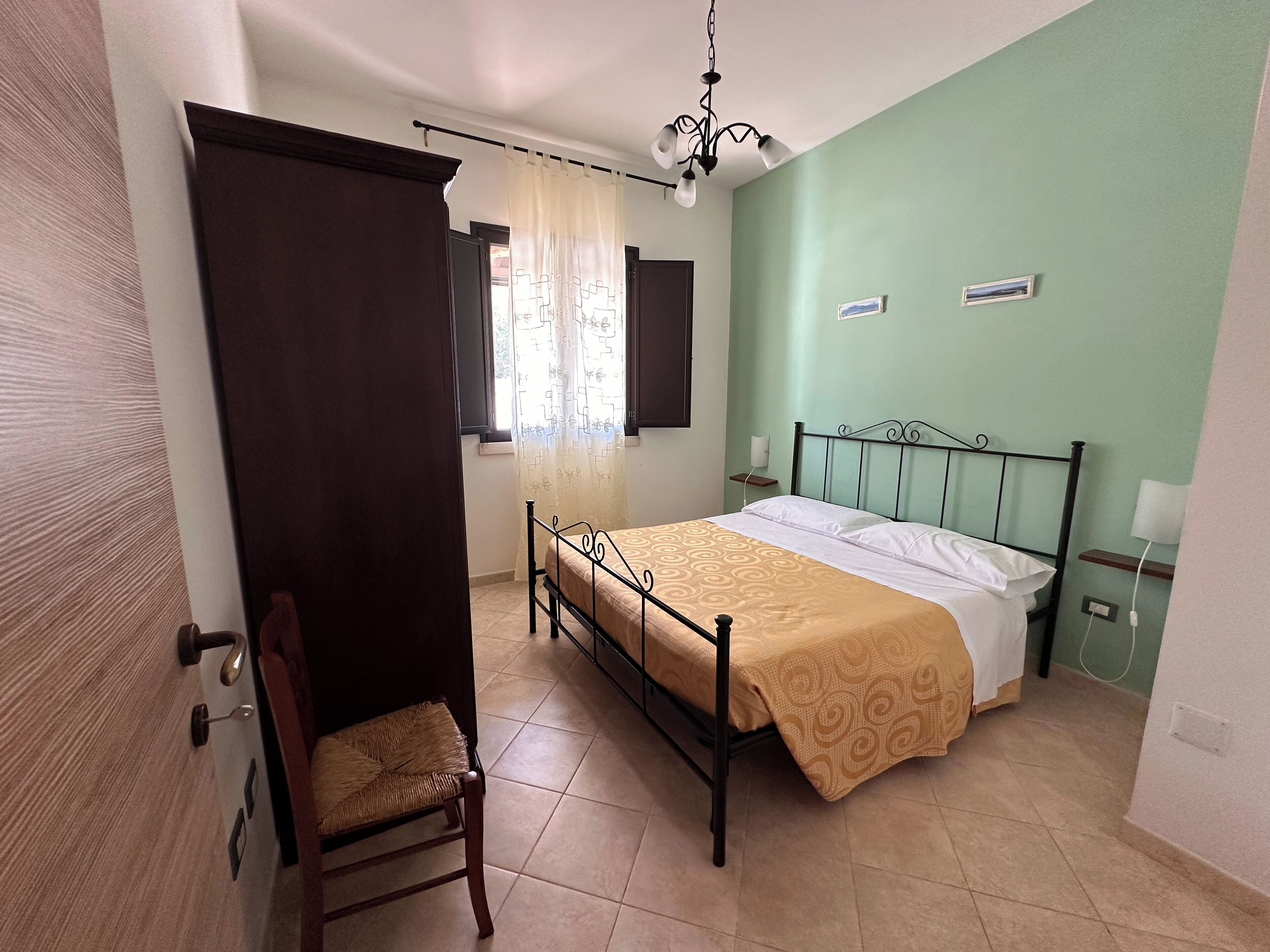 Une chambre à coucher comprenant un lit, une chaise, une fenêtre avec des rideaux, une table de chevet et un climatiseur fixé au mur.