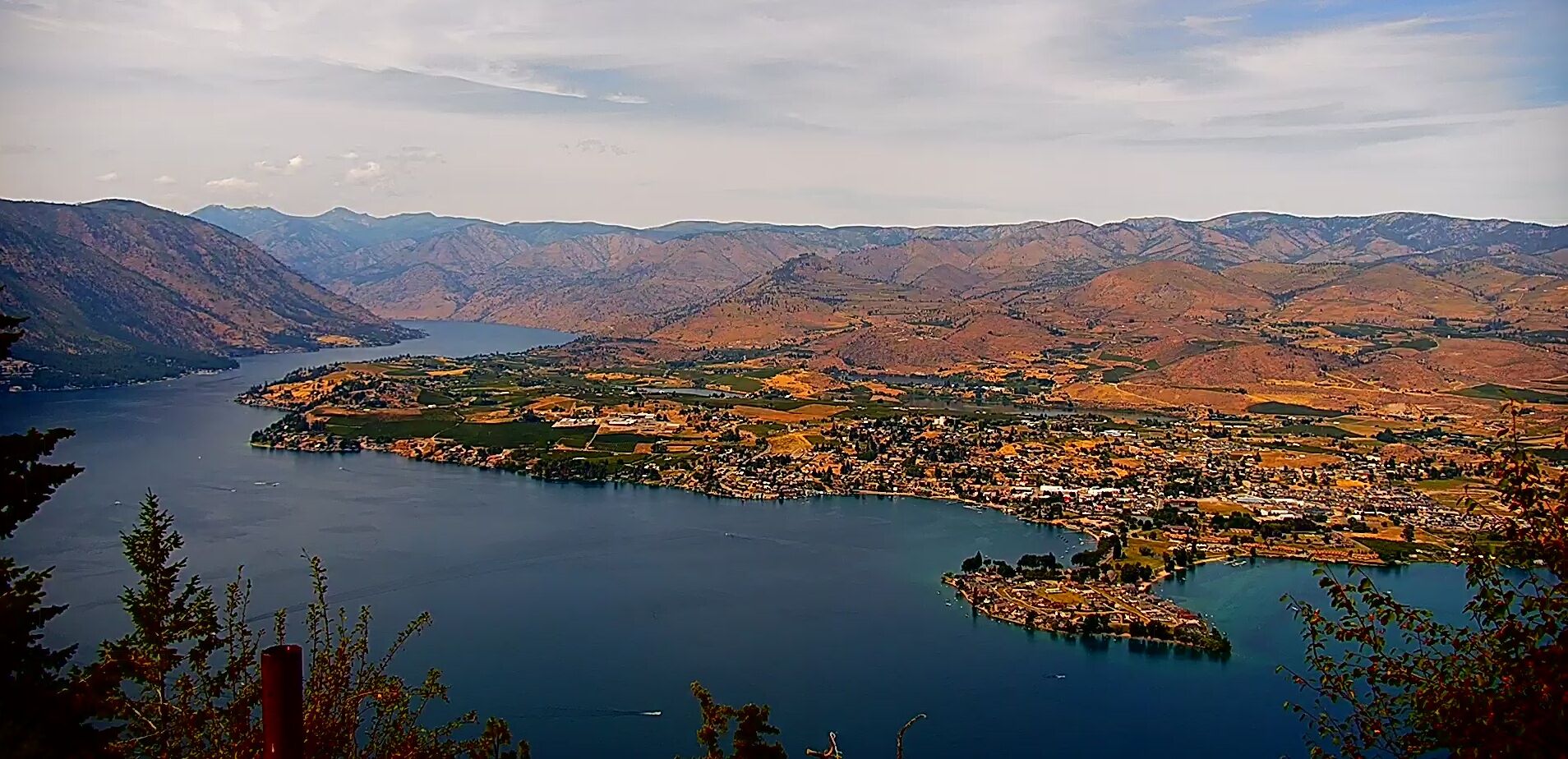 A panoramic view of a town by a lake with surrounding mountains.