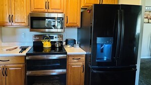 A kitchen with wooden cabinets, stainless steel appliances including a microwave, oven, and refrigerator, and a kettle on the stove.